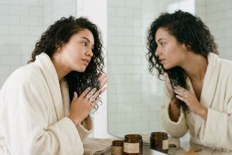 Jeune femme aux cheveux bouclés indisciplinés appliquant un masque capillaire dans une salle de bain moderne